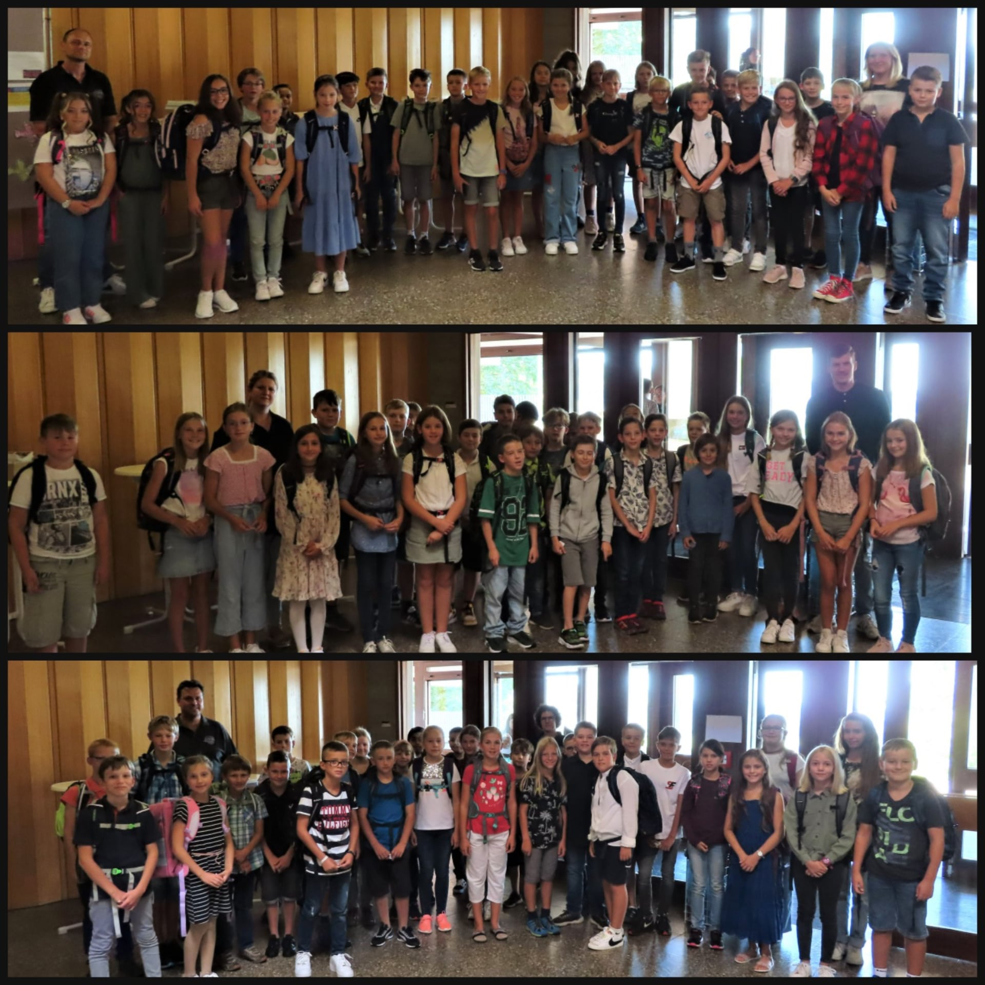Drei Gruppen Schulkinder mit Rucksäcken und Lehrkräften in einem Schulflur stehend, Blick zur Kamera