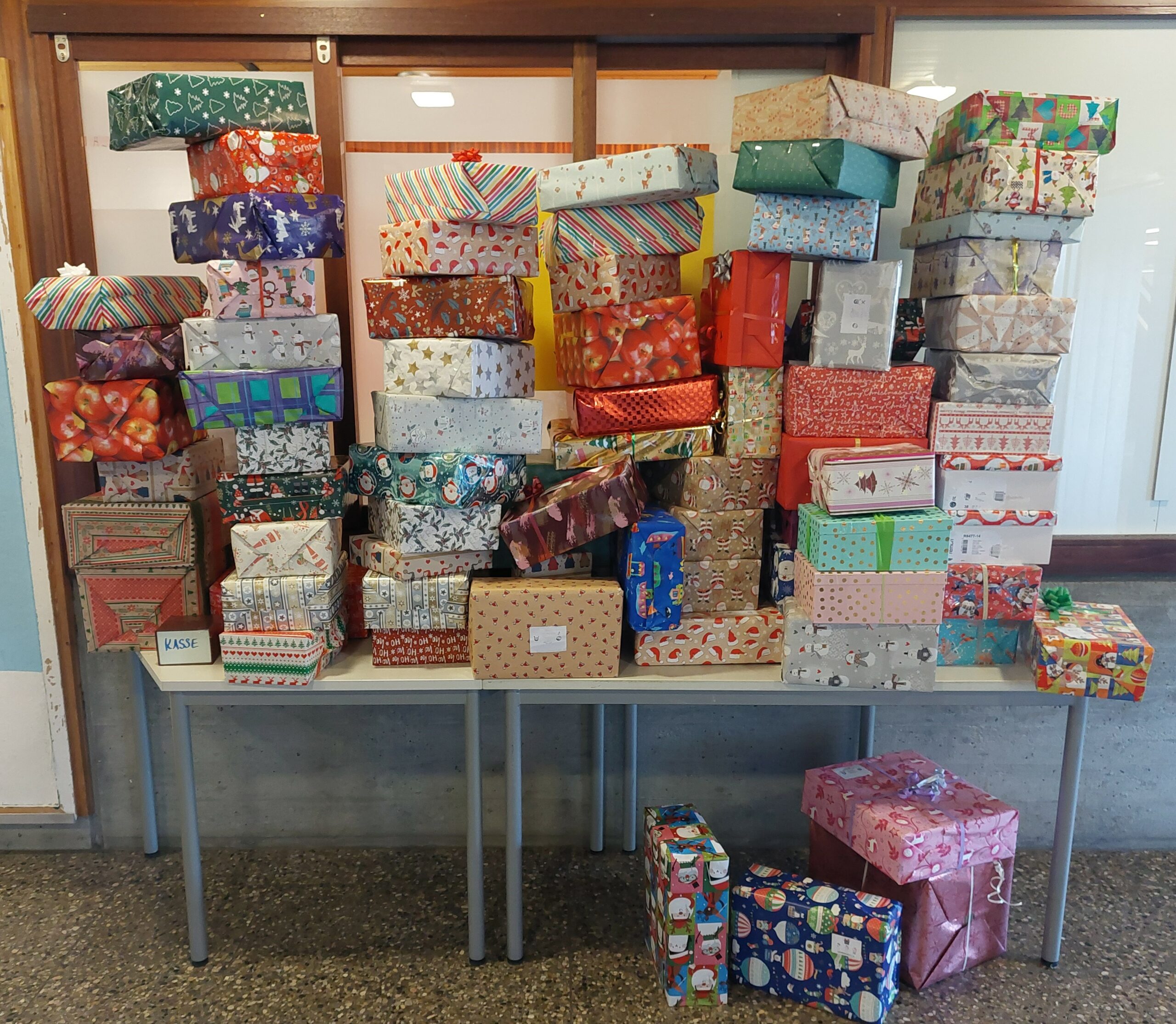 Viele bunt verpackte Geschenke gestapelt auf Tischen, weihnachtliche Muster und Schleifen.