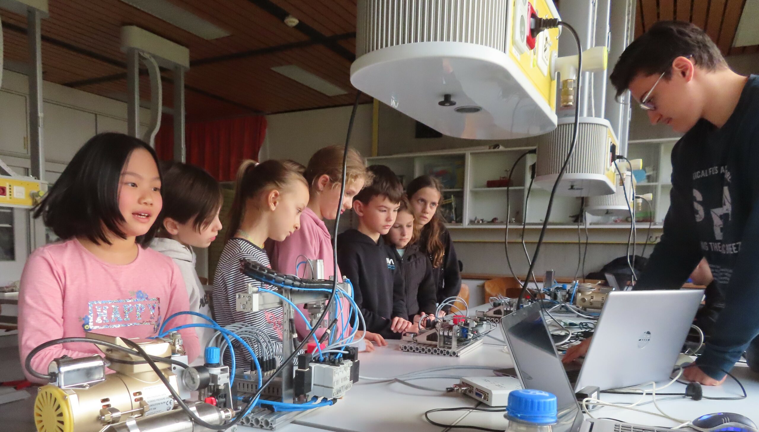 Mehrere Kinder beobachten an einem Arbeitstisch elektronische Versuchsaufbauten, Betreuer arbeitet am Laptop.