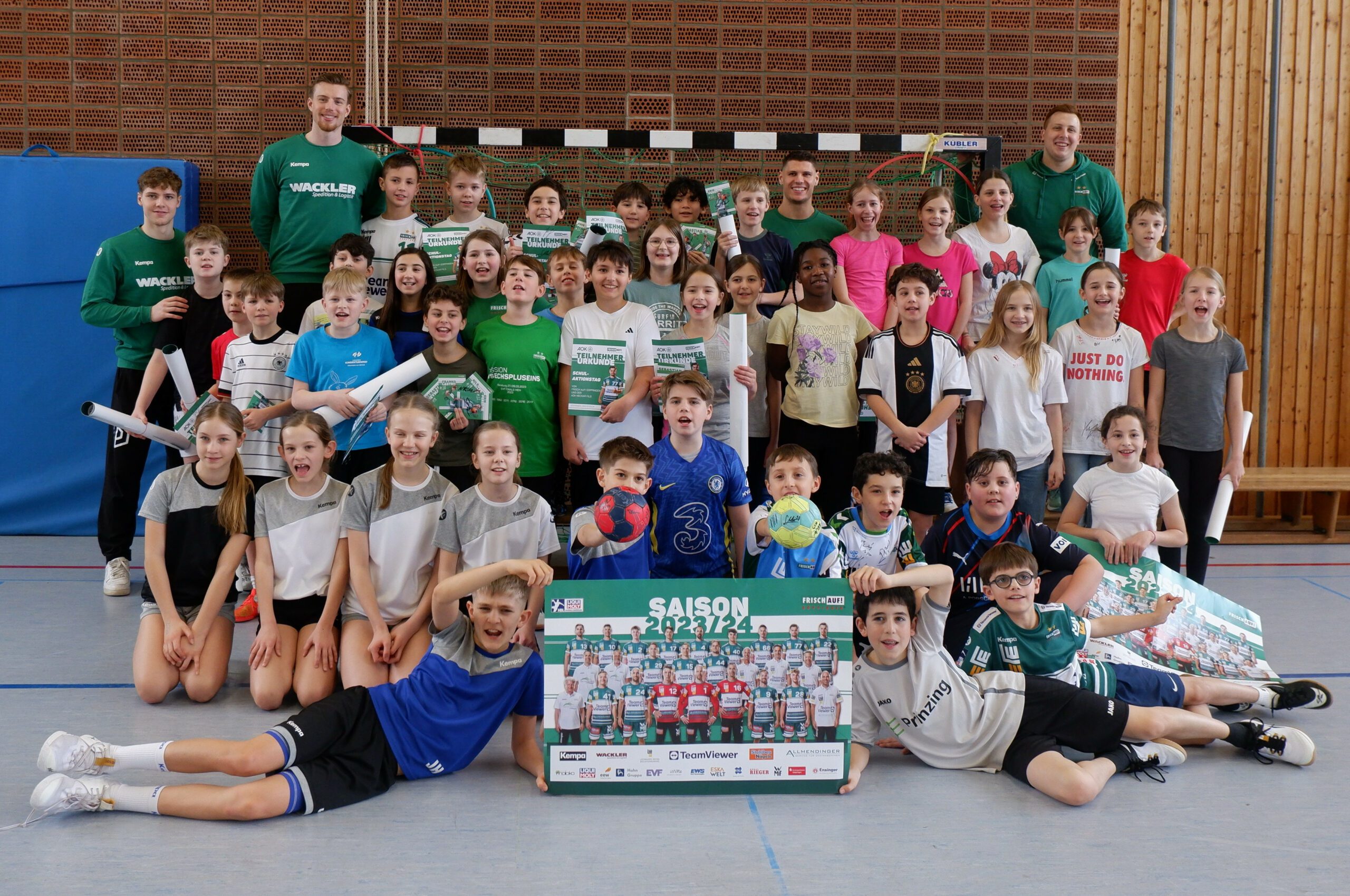 Gruppenfoto: Kinder und Trainer in Sporthalle mit Handbällen, Urkunden und Saisonposter
