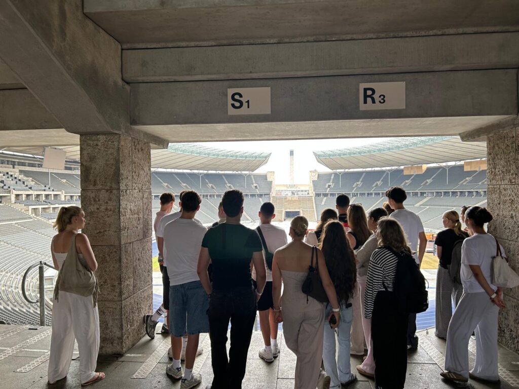 Gruppe steht unter Betonüberhang an Eingang S1/R3 und blickt auf leeres Stadion mit Tribünen