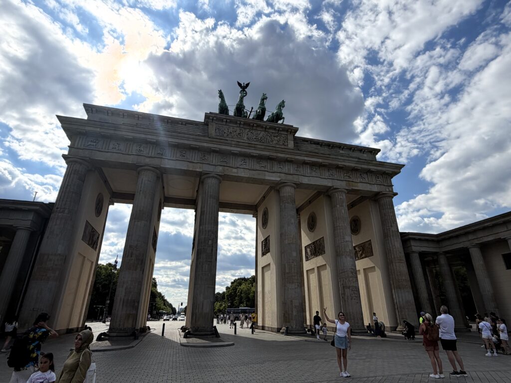 Brandenburger Tor in Berlin mit Quadriga über Säulen, Menschen im Vordergrund und dramatischem Wolkenhimmel
