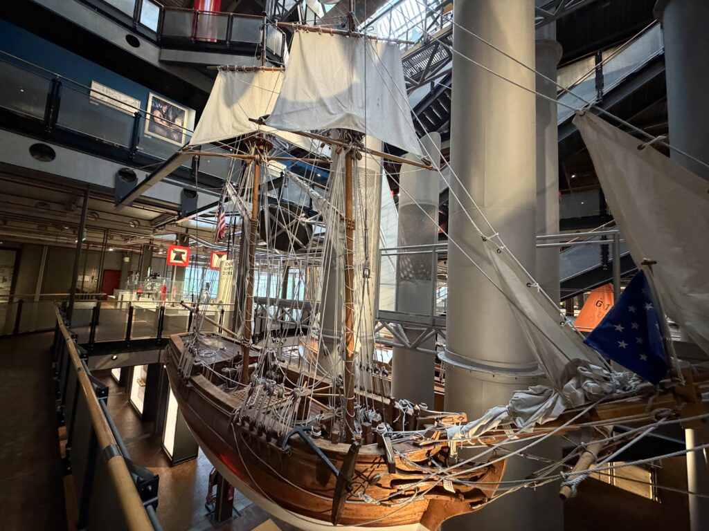 Historisches Segelboot mit weißen Segeln und komplexer Takelage in großräumiger Museumshalle, Blick von oben