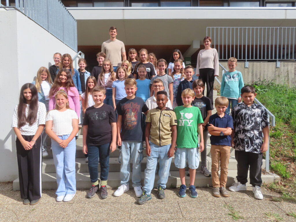 Schulklasse auf Treppenstufen vor Gebäude, etwa 25 Kinder in Reihen mit zwei Lehrern