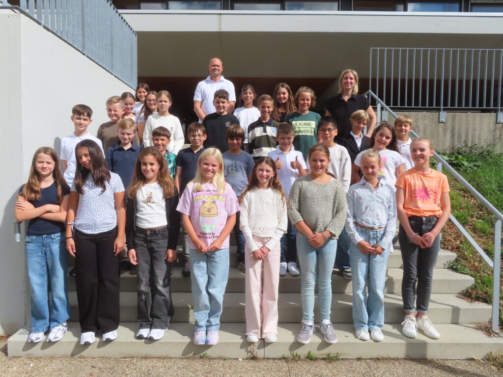 Schülerinnen und Schüler mit zwei Lehrkräften auf Außentreppen vor einem Schulgebäude, Gruppenfoto.
