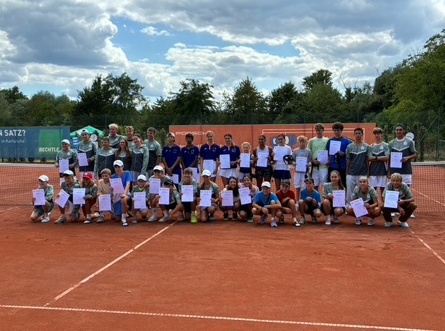 Kinder und Jugendliche als Tennisspieler auf rotem Sandplatz halten Zertifikate und posieren vor bewölktem Himmel.